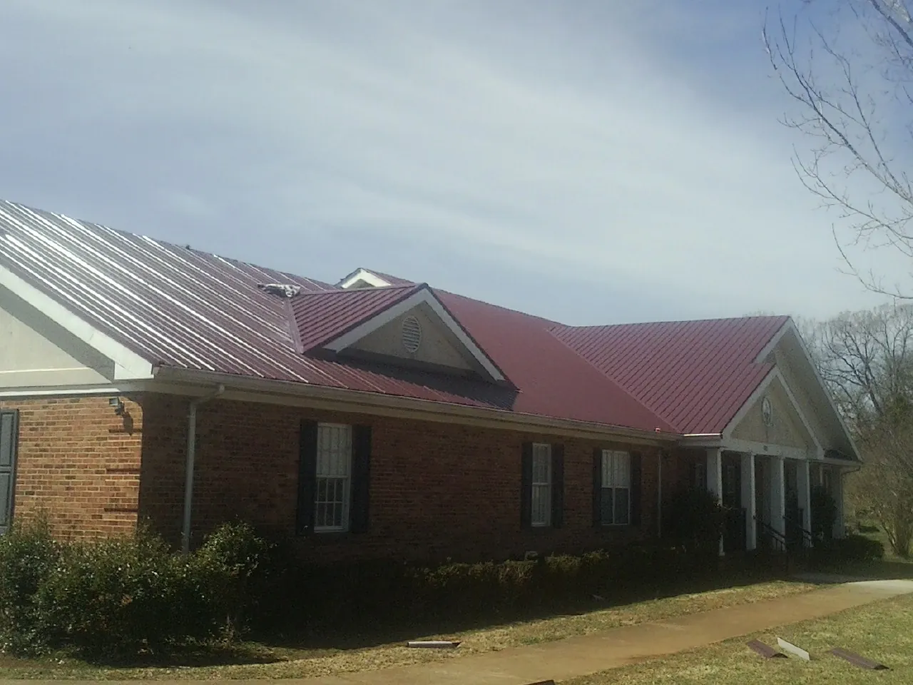 Red metal roof with gabled entries on a long brick building, from a Hail Damage Roof Repair job in Kirkman