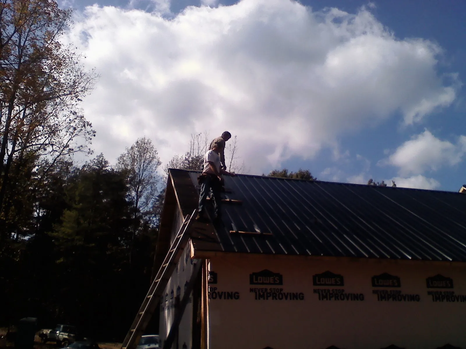Roofer fastening dark metal panels high against a cloudy sky, from a Roof Inspection job in Kirkman
