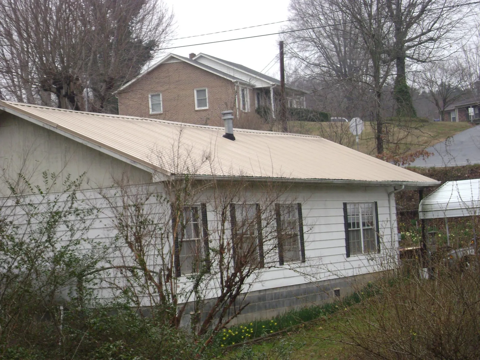 Tan metal roof on a white sided house set into a hillside — Commercial Roofing by Roofing Brothers in Kirkman